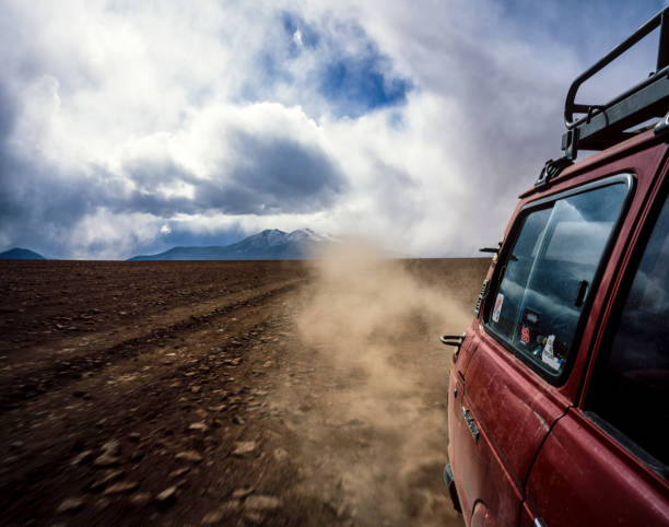 Altiplano, Bolivia - March 2006: Red jeep driving along a dirt road and kicking up dust on the Altiplano in Bolivia, with mountains in the background