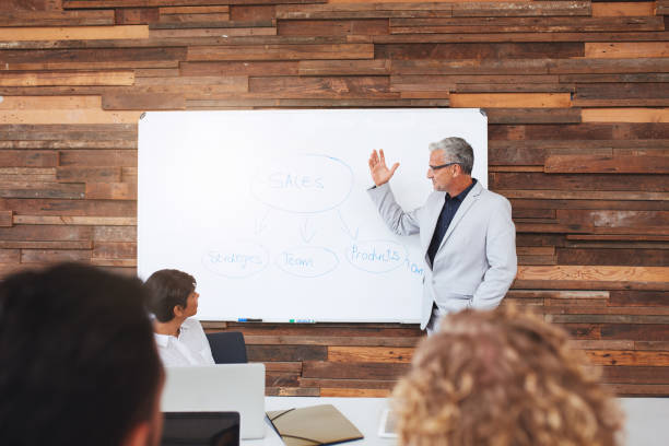 istock Mature businessman presenting ideas on a whiteboard to office colleagues 1180533824