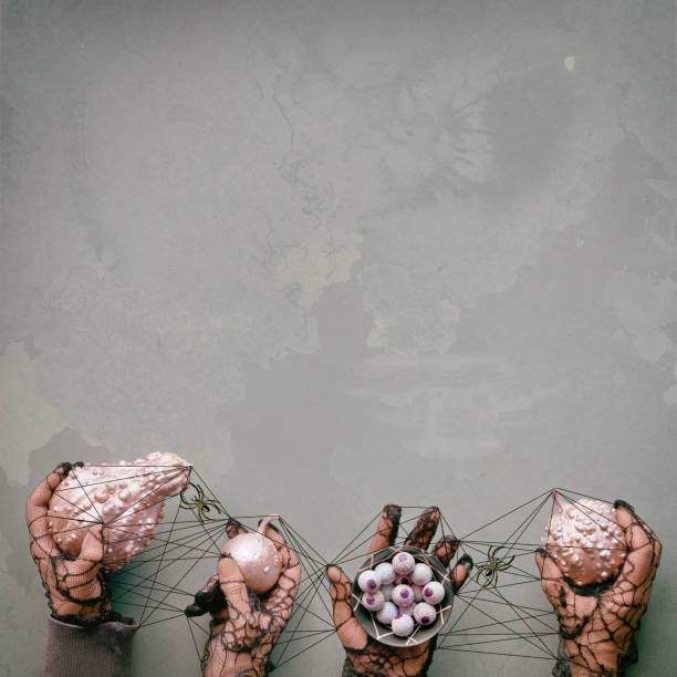 Creative Halloween background. Hands in black mesh gloves hold pink decorative pumpkins and chocolate eyes. Hands are tied up with black string in cat's cradle with spiders.