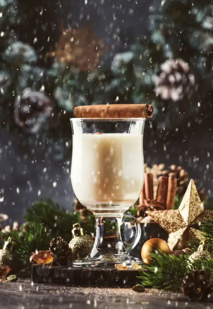 Christmas or New Year Eggnog alcoholic cocktail - hot winter drink with milk, eggs and rum, sprinkled with cinnamon and nutmeg in glass on gray background, copy space