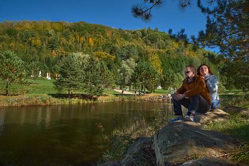 couple of tourists by the lake enjoy nature in a Buddhist temple in Quebec on a sunny day.