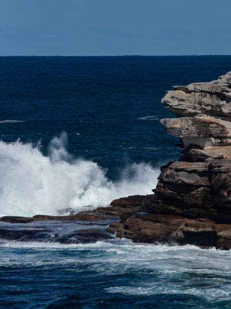 istock Oceanside rocky sandstone cliff with blue sea water waves creating whitewash against coastline and clear sky in background 1180543217