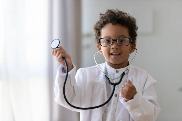Cute african kid boy wear medical uniform playing doctor, portrait Cute small african american kid boy wear medical uniform glasses holding stethoscope playing doctor, happy funny little mixed race preschool child pretending pediatrician looking at camera, portrait theatrical performance photos stock pictures, royalty-free photos & images