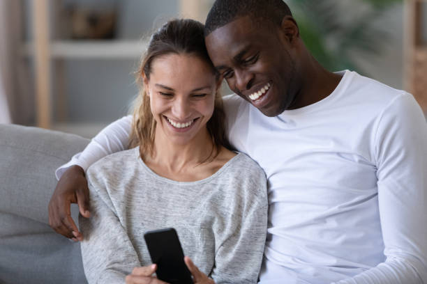 istock Happy mixed race couple using phone taking selfie on sofa 1180549303