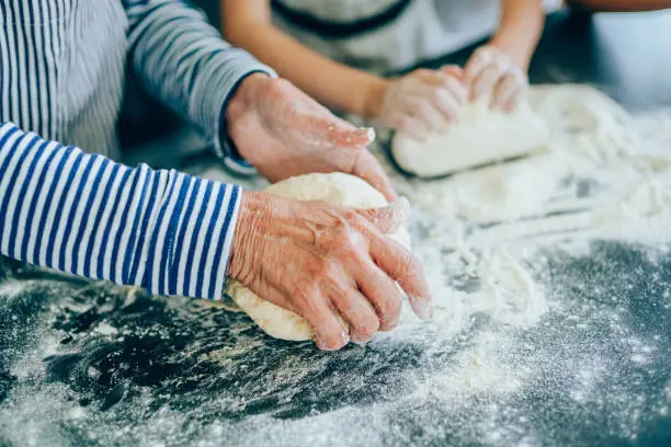 Close-up of wrinkled hands of older woman and child hands kneading dough
