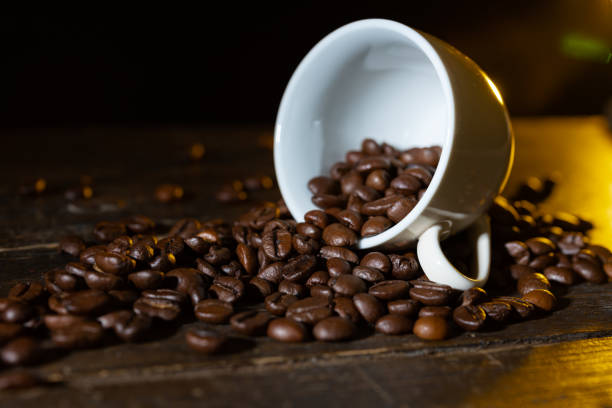 Small cup full of coffee beans on an old wooden table in fron of a drak background