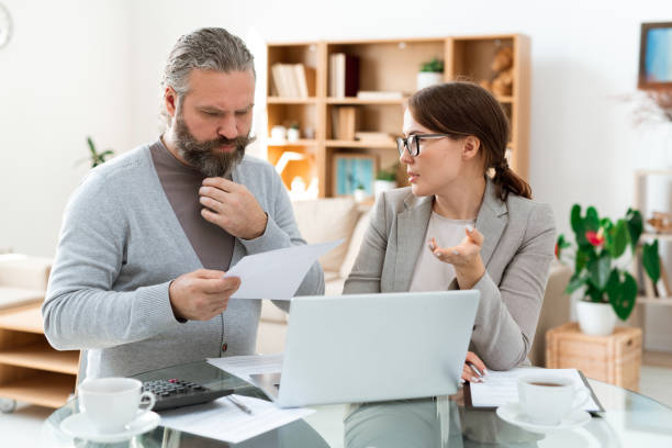 istock Pensive bearded man looking through paper while listening to real estate agent 1180557754