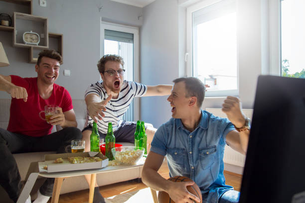 Young adult males watching basketball game and drinking beer at home stock photo