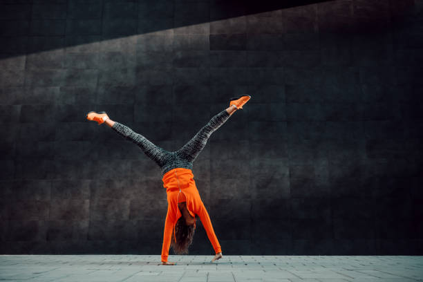 Full length of fit sporty caucasian woman in sportswear doing cartwheel exercise in front of black wall. Full length of fit sporty caucasian woman in sportswear doing cartwheel exercise in front of black wall. acrobatic activity stock pictures, royalty-free photos & images