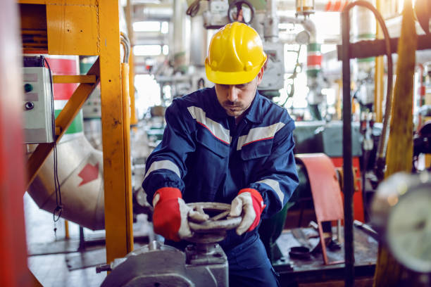 trabajador de la planta de energía trabajadora en traje de trabajo y con casco protector en la válvula de atornillado de la cabeza. - boiler power station fuel and power generation gas boiler fotografías e imágenes de stock