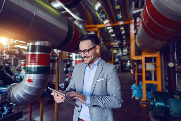 istock Handsome caucasian manager in gray suit and with eyeglasses using tablet while standing in energy plant. 1180563218