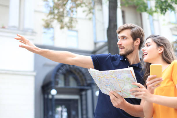 istock Beautiful young couple holding a map and smiling while standing outdoors. 1180563854