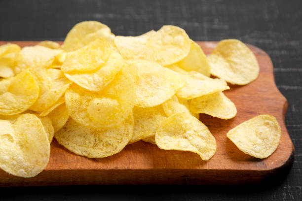istock Delicious potato chips with salt on a rustic wooden board on a black surface, side view. Close-up. 1180567002