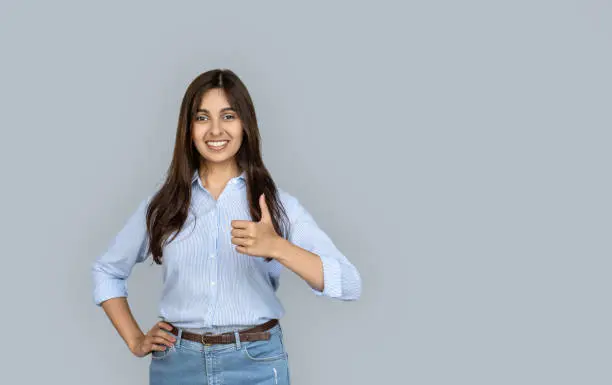 Happy young indian woman professional student satisfied customer look at camera show thumbs up like hand gesture recommend advertise good quality service stand isolated on grey background copy space