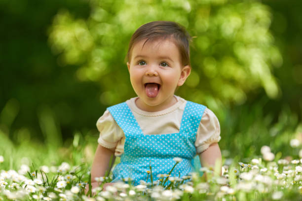 Baby girl wearing blue dress sticking out her tongue in the public park