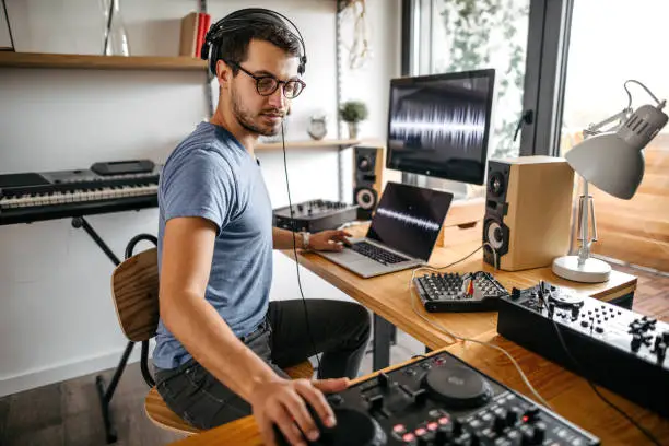 Young man recording new music using laptop and digital mixing control at home studio