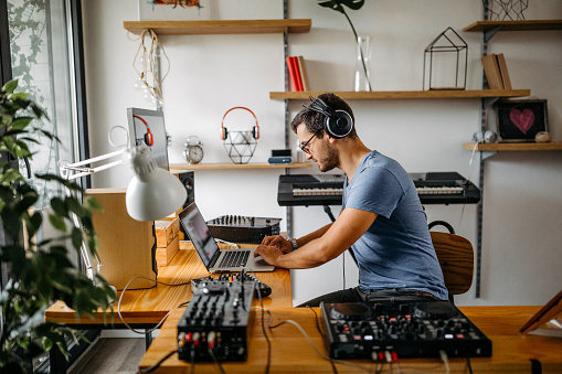 Young man using laptop while recording new music at home studio