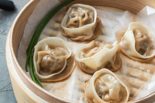 High angled view of cooked dumplings inside bamboo steamer with lip partially off.