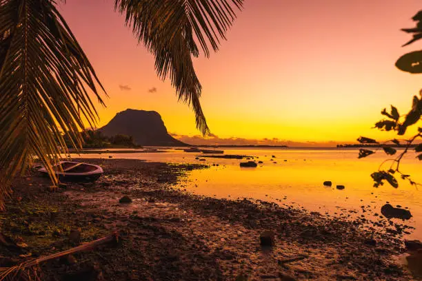 Photo of Fishing boats in a quiet ocean at sunset time. Le Morn mountain in Mauritius.