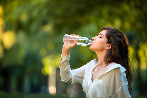 Beautiful woman drinking water from plastic bottle in nature