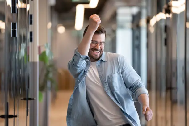 Ecstatic excited male winner dancing in office hallway laughing celebrating work achievement professional win, happy overjoyed business man enjoy victory dance euphoric about success reward promotion