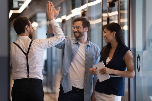 Friendly male colleagues giving high five talking in office hall Friendly male colleagues giving high five talking standing in office hall, smiling businessmen diverse professionals group greeting meeting in company hallway work space express respect agreement office buddies stock pictures, royalty-free photos & images