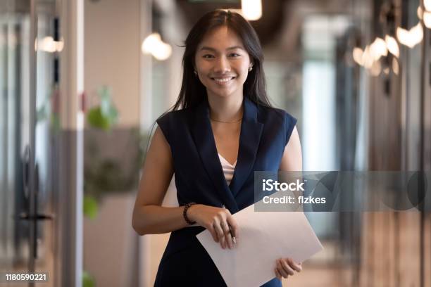 Happy Asian Businesswoman Looking At Camera Stand In Office Hallway Stock Photo - Download Image Now