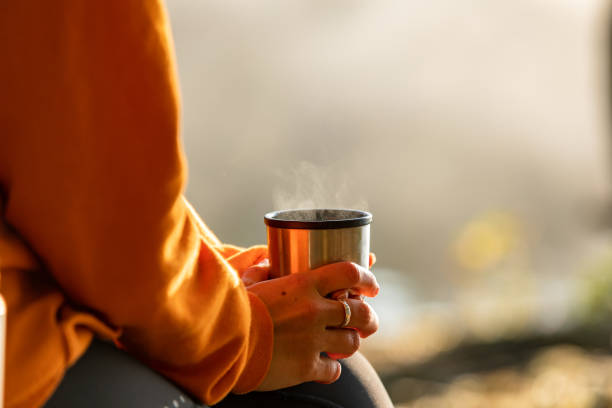 Morning coffee outdoors A woman wearing sports clothes is sitting on a bench outdoors holding a cup of coffee. The image is a close-up of her hands holding the cup. flask stock pictures, royalty-free photos & images