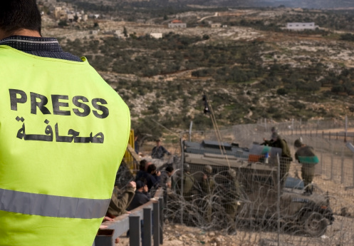 A journalist wears a clearly marked vest near military in the West Bank