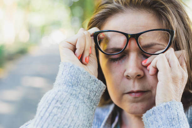 Woman rubbing her eye outdoors Close up shot of young woman rubbing her eye with one hand outdoors - Portrait of cute and sleepy girl with brown hair wearing eyeglasses nose flower stock pictures, royalty-free photos & images