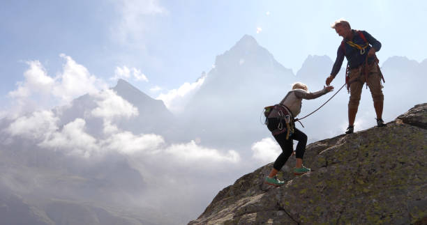 les couples mûrs montent la crête de roche, utilisant la corde - climbing mountain climbing rock climbing moving up photos et images de collection