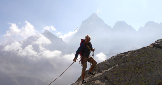 l'homme mûr grimpe la crête de roche, utilisant la corde - mountain climbing rock climbing motivation awe photos et images de collection