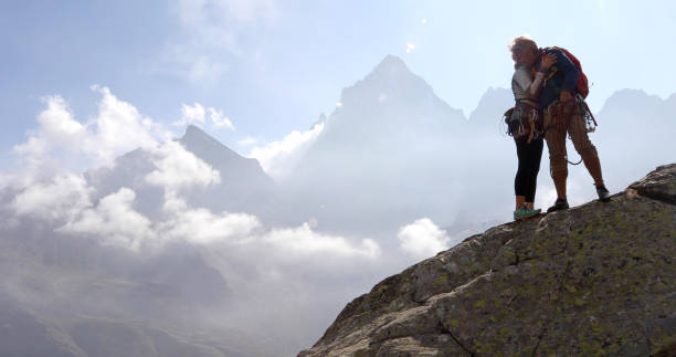 istock Mature couple exchange hug on rock ridge, summit 1180596589