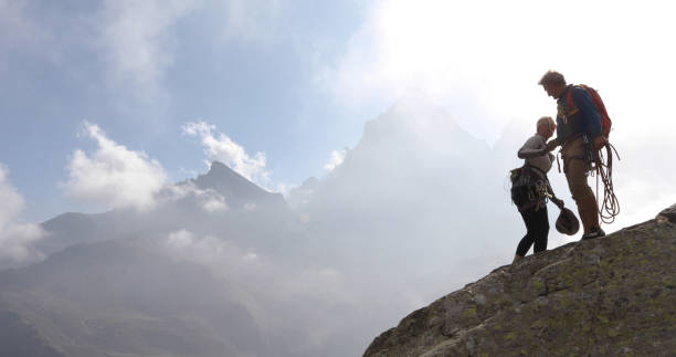 les couples mûrs montent la crête de roche, arrivent au sommet - mountain climbing rock climbing motivation awe photos et images de collection