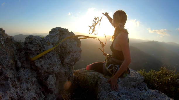 young woman prepares to descend, throws rope from summit - climbing adventure moving up clambering imagens e fotografias de stock