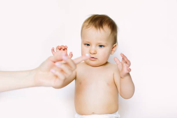 Young mother applying face kids cream on her baby girl face against light background. Hygiene, healthcare concept Young mother applying face kids cream on her baby girl face against light background. Hygiene, healthcare concept. creaming stock pictures, royalty-free photos & images