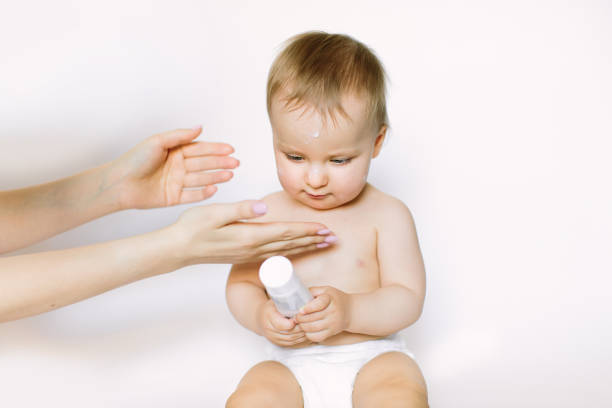 Mother hands applying cream on baby after bathing on white background. The baby holds the tube with a cream in her hands Mother hands applying cream on baby after bathing on white background. The baby holds the tube with a cream in her hands. creaming stock pictures, royalty-free photos & images