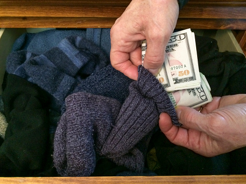 Money in a sock drawer. $50 bills rolled up and being put into a sock. Socks are in a dresser drawer. This is in our home, taken with a cell phone. mobilestock. Taken on mobile device.