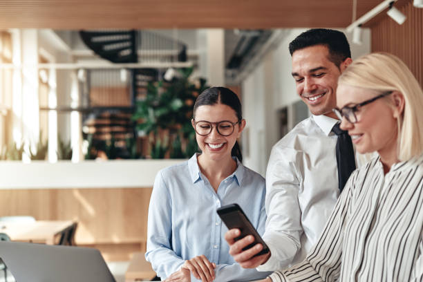 istock Three smiling businesspeople using a cellphone together in an office 1180599551