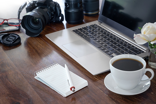 workplace of a photographer with laptop, camera, lenses coffee cup and notepad on a wooden table,  copy space, selected focus, narrow depth of field