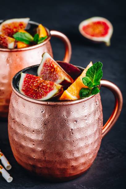 Fig moscow mule ice cold cocktail in copper cup with oranges and mint