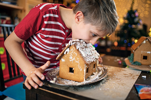 Little boy was building and decorating gingerbread house for Christmas. But the spell of freshly baked gingerbread was too much and the boy is starting to eat the house before even finishing decorating it.\nNikon D850.