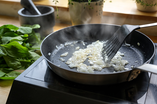 onions are fried with a lot of steam in a black pan, cooking and kitchen concept, selected focus