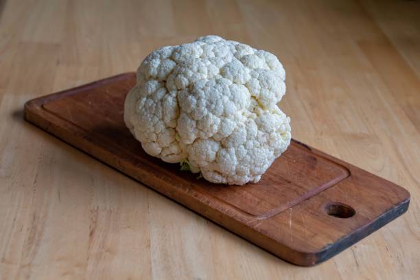 istock Cauliflower with a cutting board on a light wood table. 1180605880