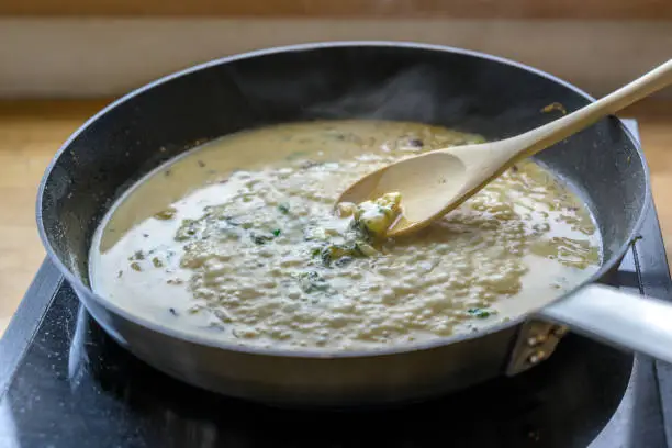 boiling gorgonzola cheese sauce in the pan on a mobile stove is stirred with a wooden spoon, cooking concept, selected focus, narrow depth of field