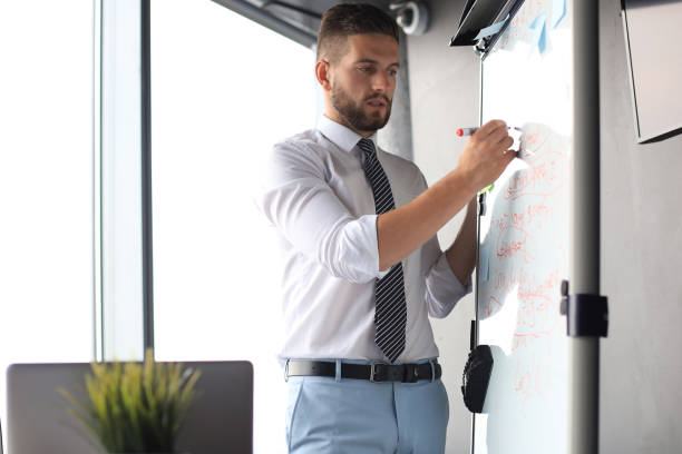 istock Smart concentrated businessman writing something on the flipchart using marker 1180613884