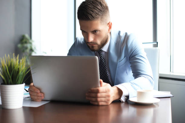 istock Good looking business man is holding laptop while sitting in the office 1180613928