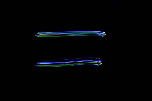 Photo of Long exposure photograph of an equals symbol in neon blue and multi colour in an abstract swirl, parallel lines pattern against a black background. Light painting photography.