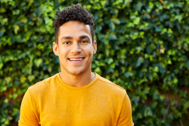 Portrait of young man in yellow t-shirt at backyard Portrait of smiling young man standing against plants. Confident male is in back yard. He is wearing yellow t-shirt. young men stock pictures, royalty-free photos & images