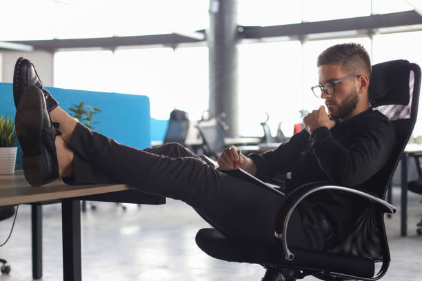 istock Focused modern businessman working and taking notes in his modern office, legs on desk 1180616594